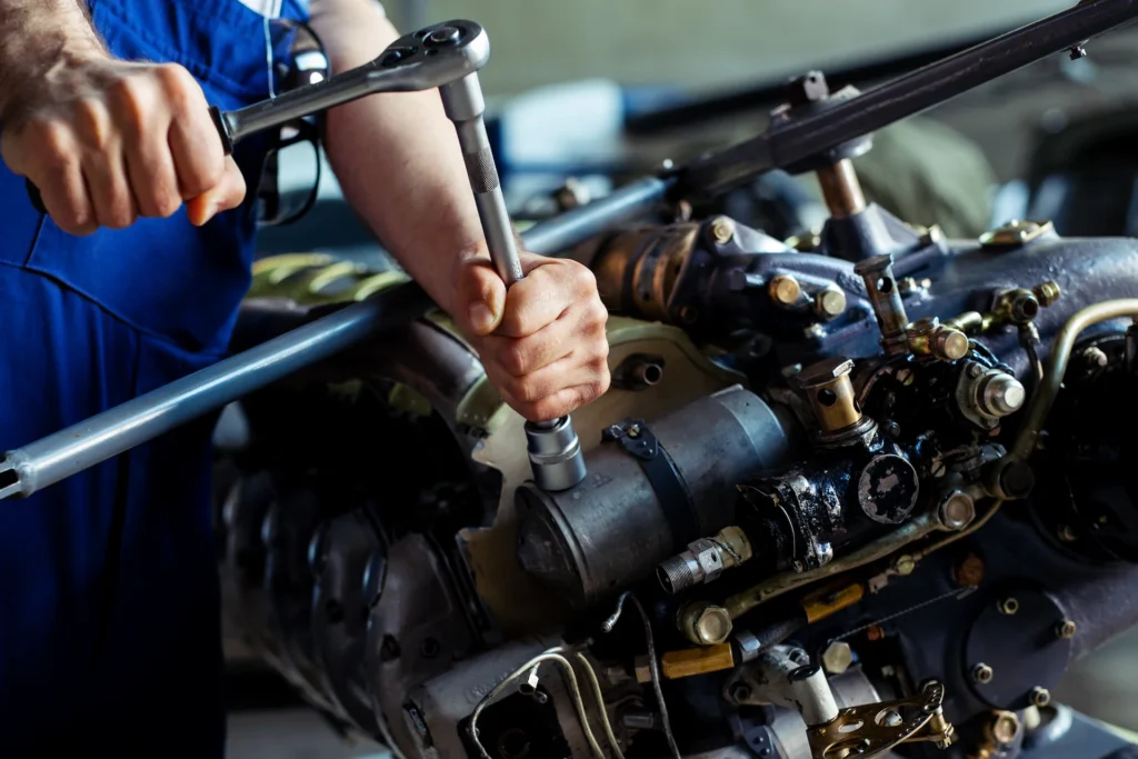 A person in blue overalls uses a large wrench to tighten a bolt on a complex engine, focusing on mechanical repair work.
