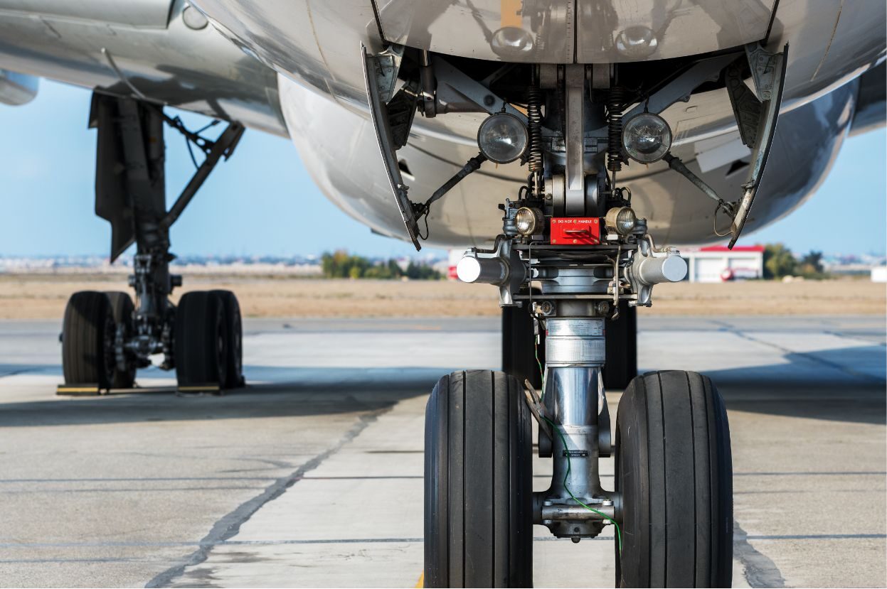 Close-up of an airplane's landing gear, showcasing tires, brake system, and hydraulic components against a runway backdrop.